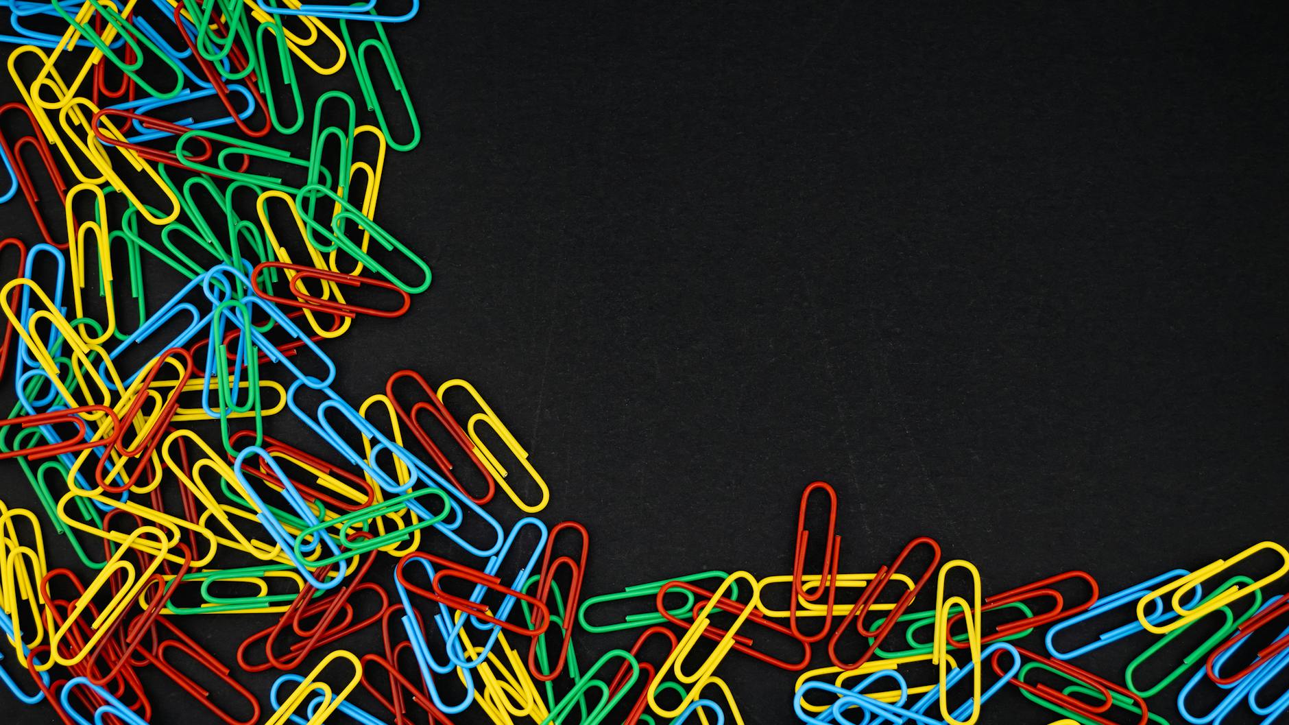 A scattered pile of colorful paperclips on a black background, offering copyspace.