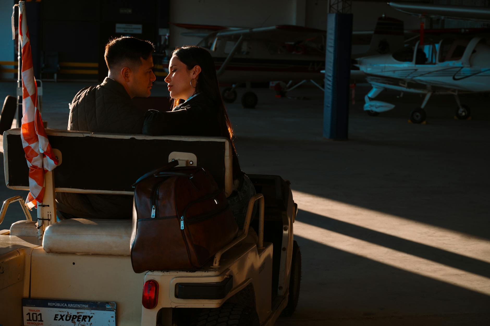 Couple sharing a moment in an aircraft hangar next to small planes at sunset.