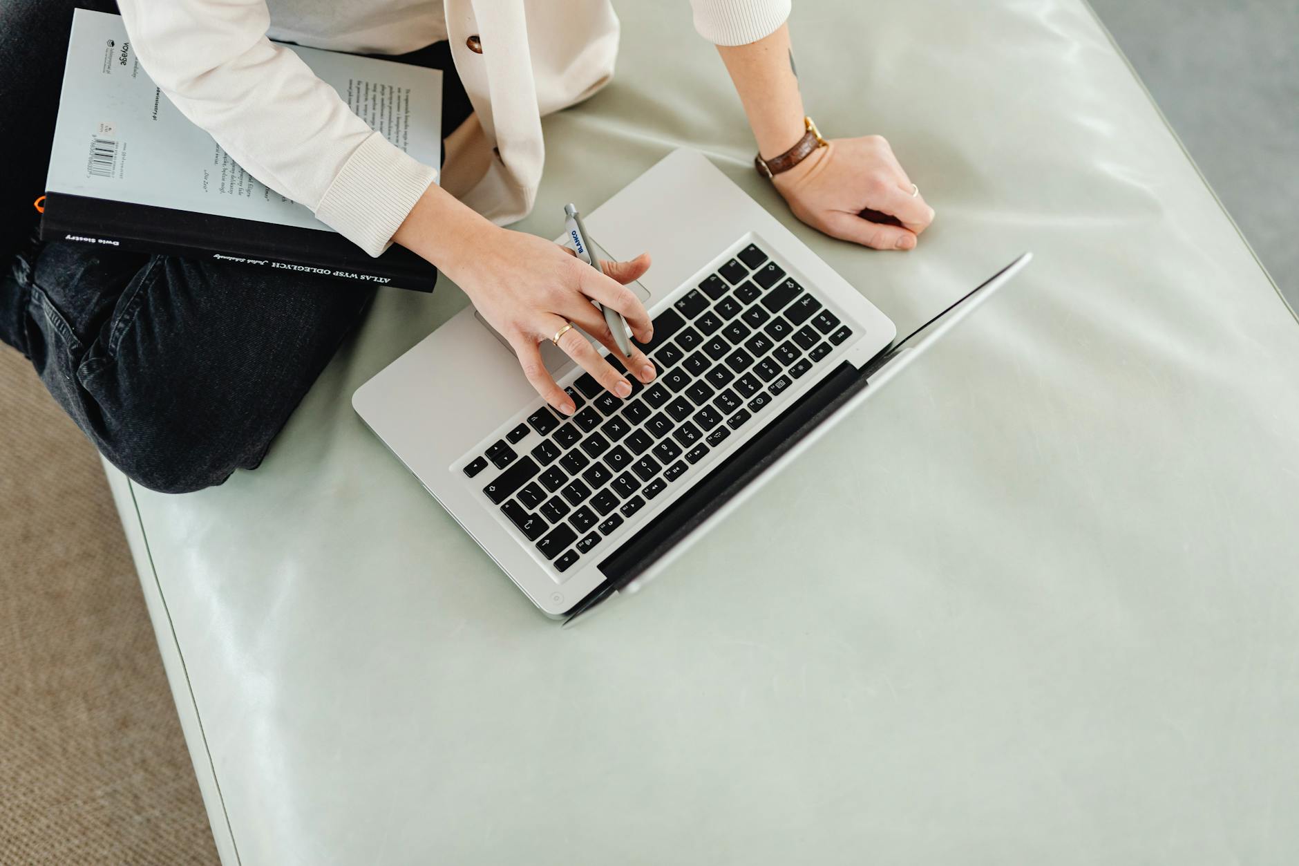 Person working remotely on a laptop with a notebook and pen in hand.
