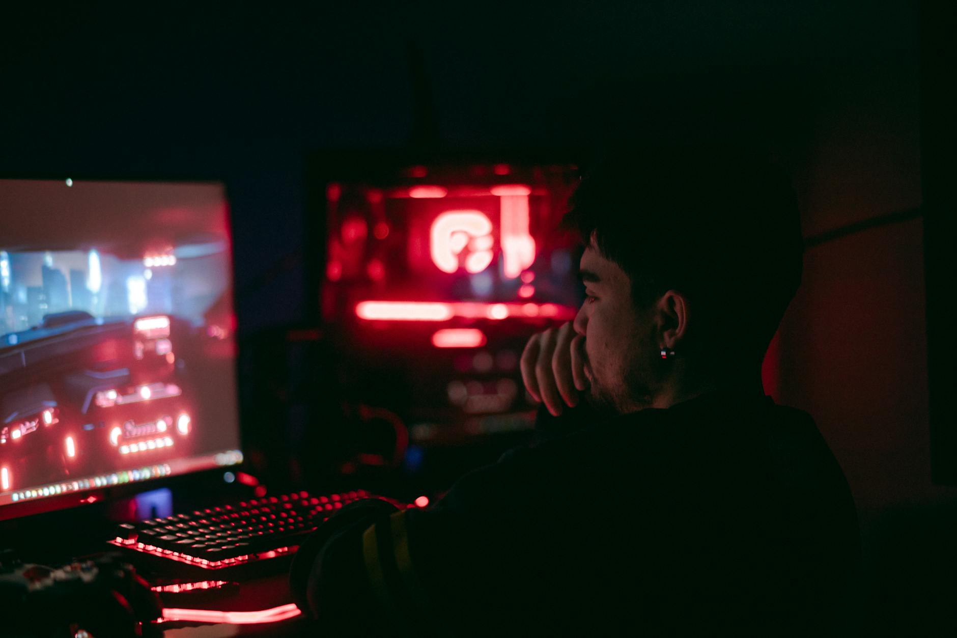 Man playing a video game on a desktop with glowing red and blue lights.