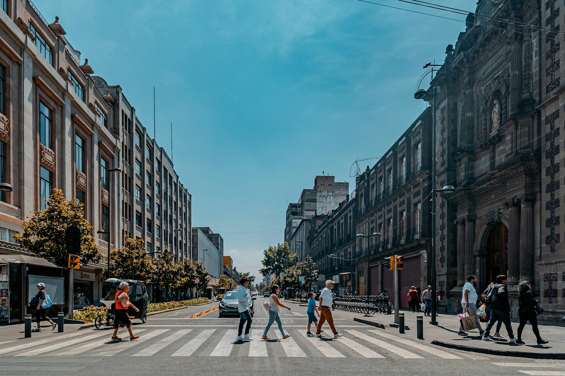 Pedestrians crossing a vibrant street in Ciudad de México under a clear blue sky.