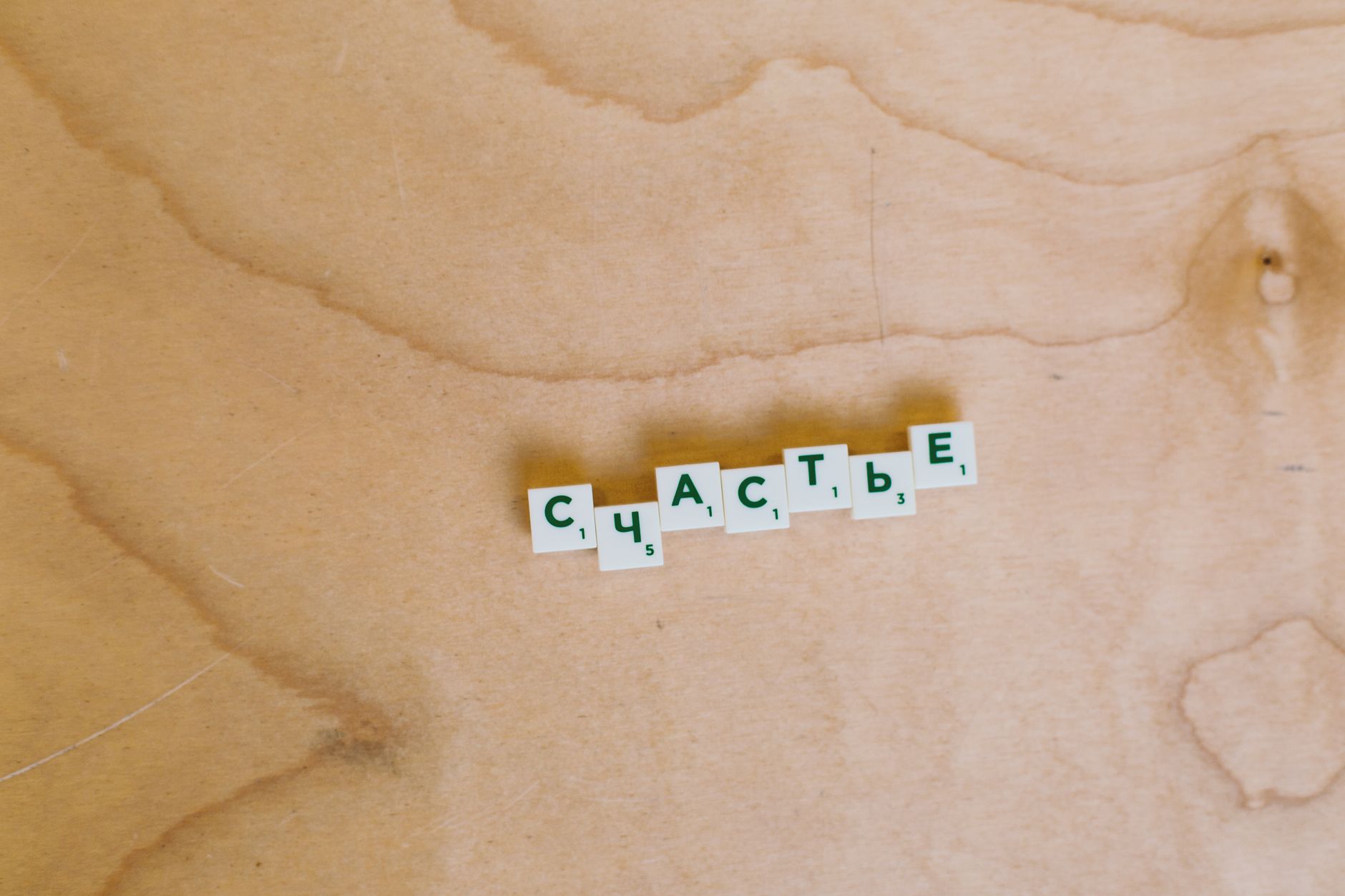 Scrabble tiles spelling 'Happiness' in Cyrillic on a light wooden surface.