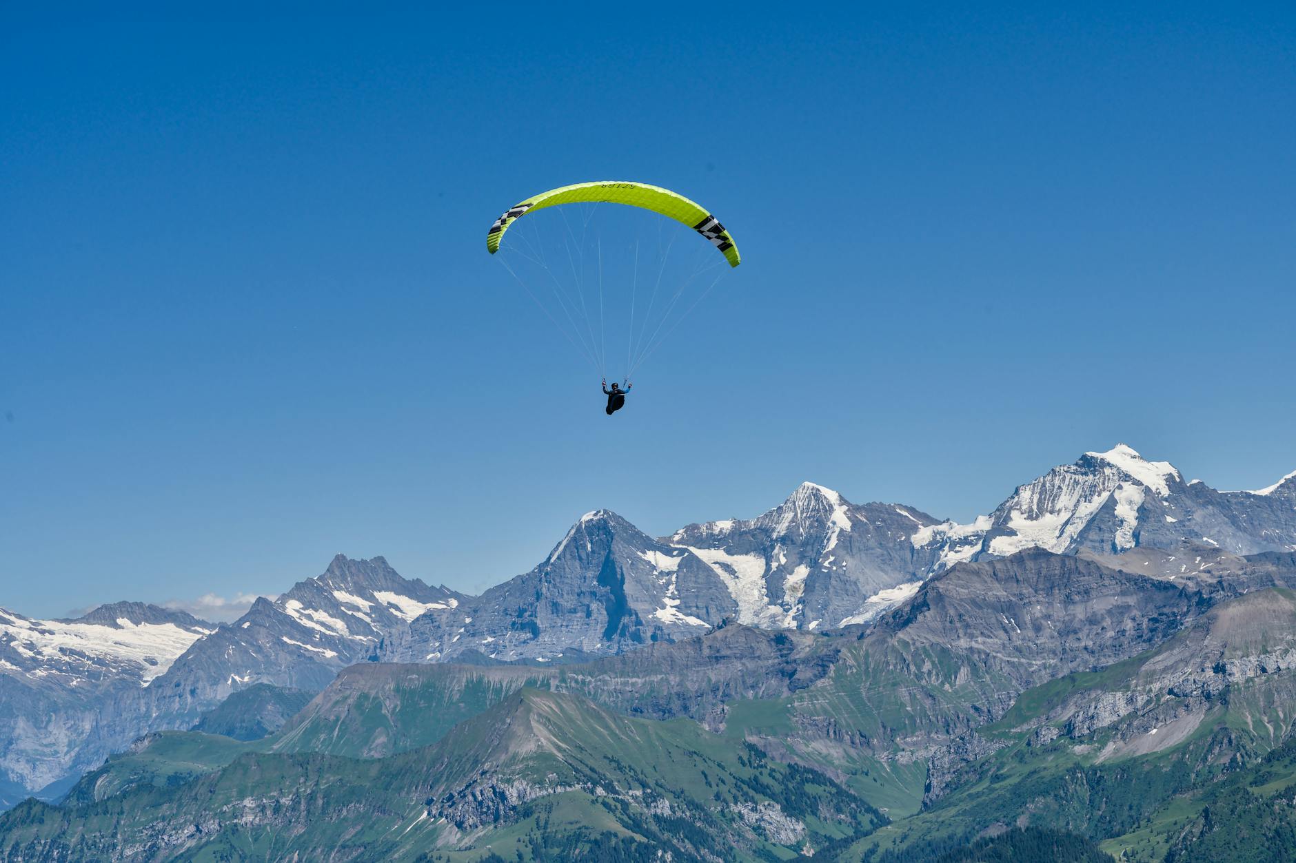 Paraglider soaring over the stunning Swiss Alps on a clear summer day.