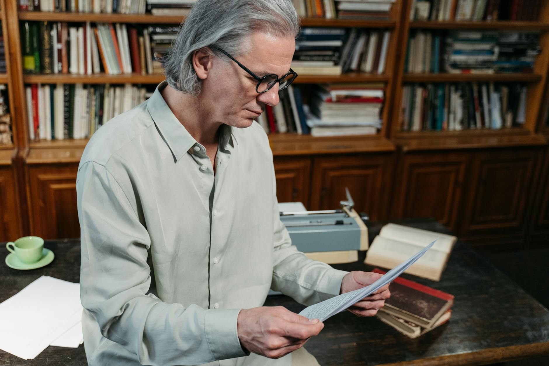 Senior man with gray hair reading documents in a cozy library.