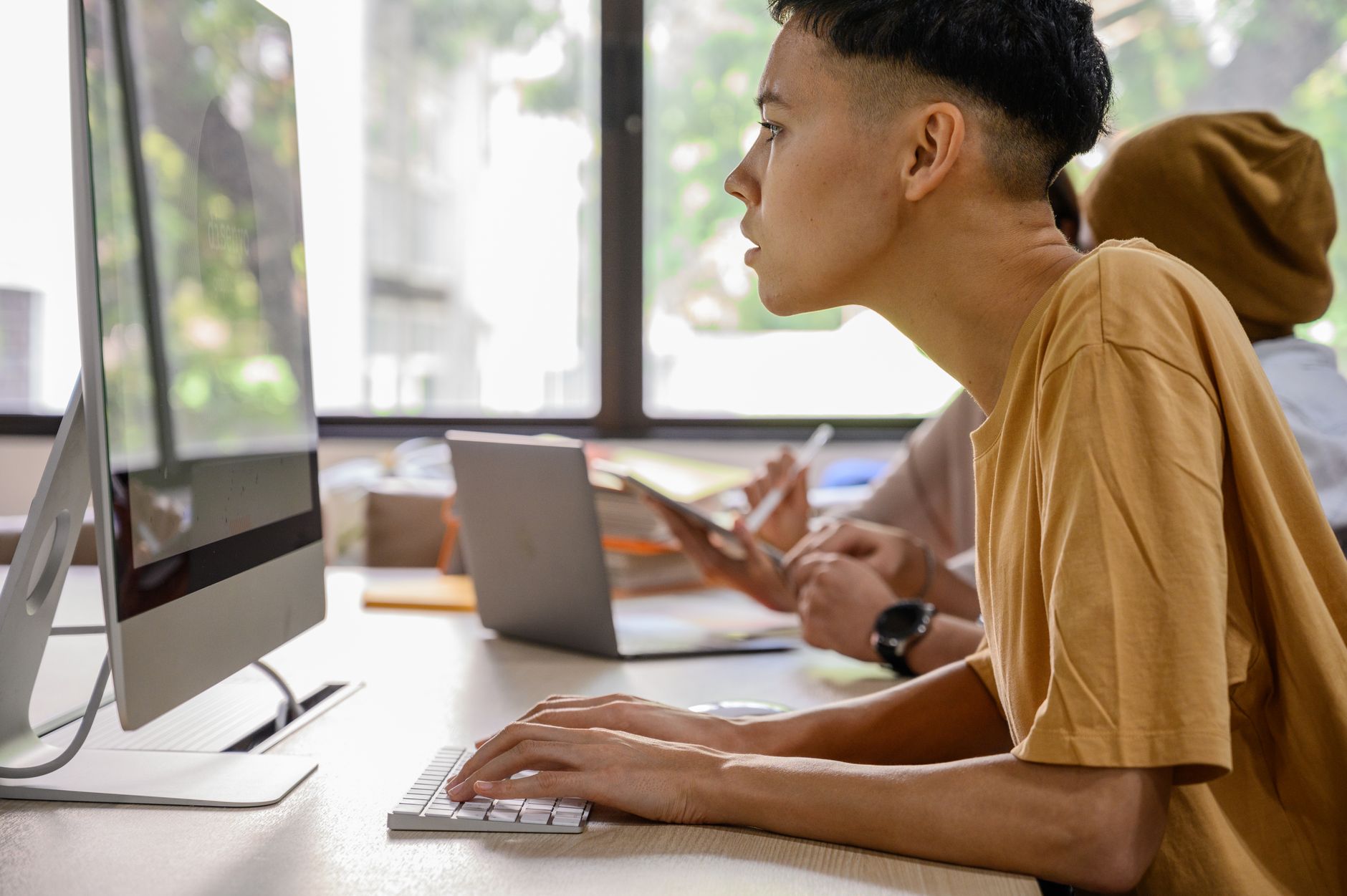 Diverse young adults engaged in work at desks with computers in a modern office.