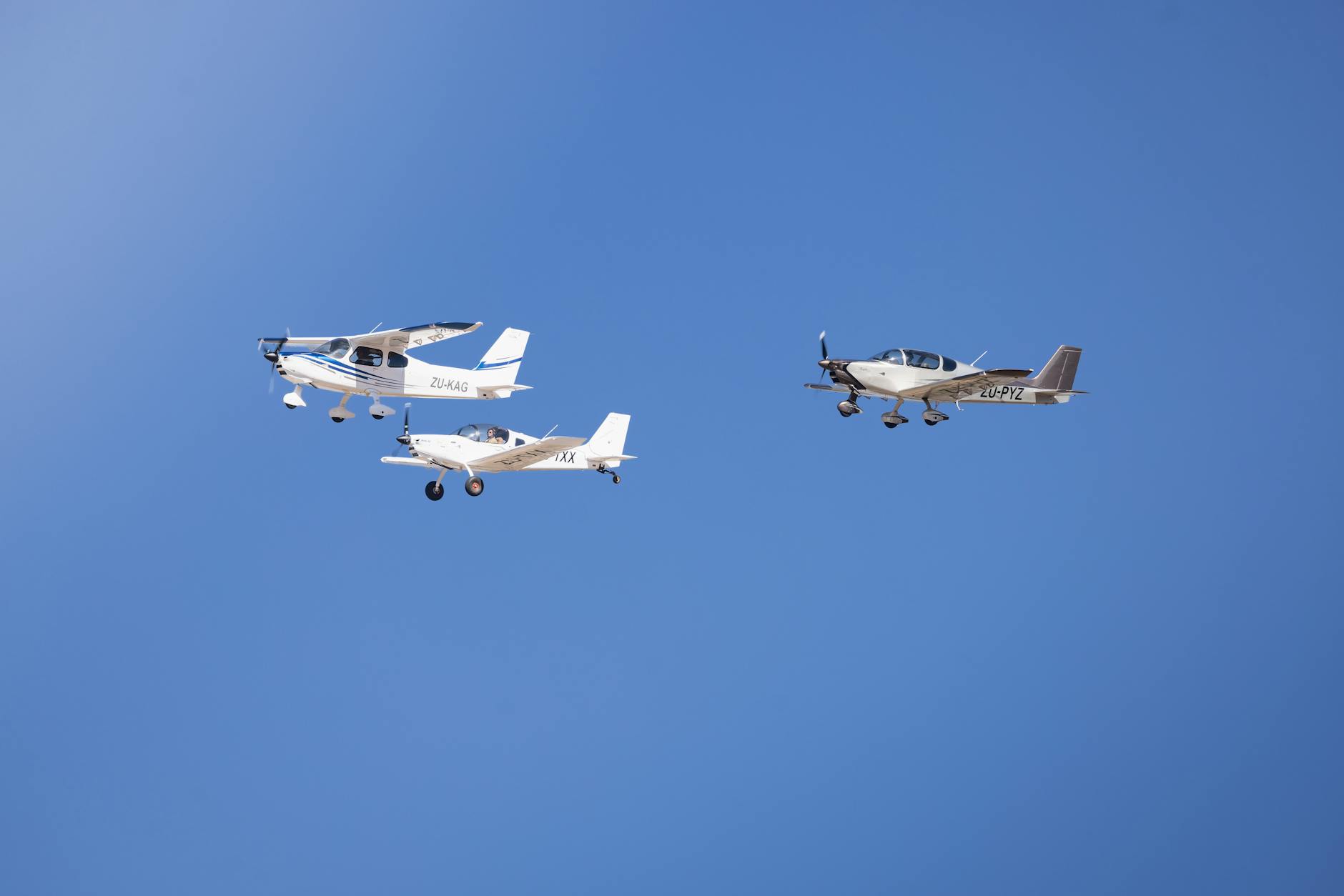 Three light aircraft flying in formation against a clear blue sky, showcasing aviation precision.