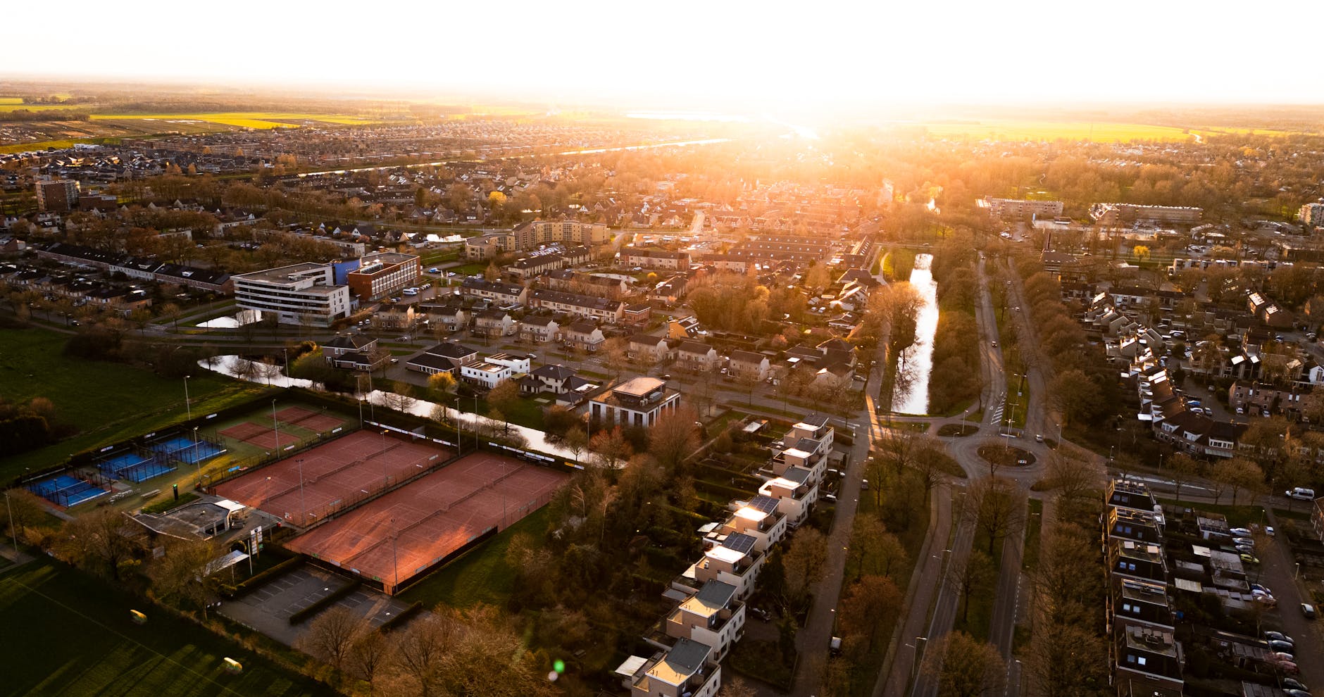 Aerial view of Hoogeveen at sunset highlighting urban architecture, tennis courts, and streets.