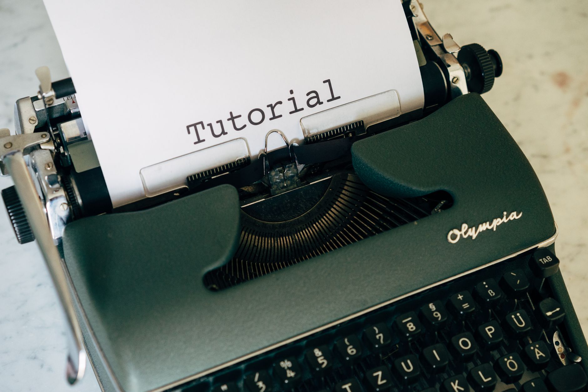 Close-up of a vintage Olympia typewriter with paper displaying 'Tutorial'.