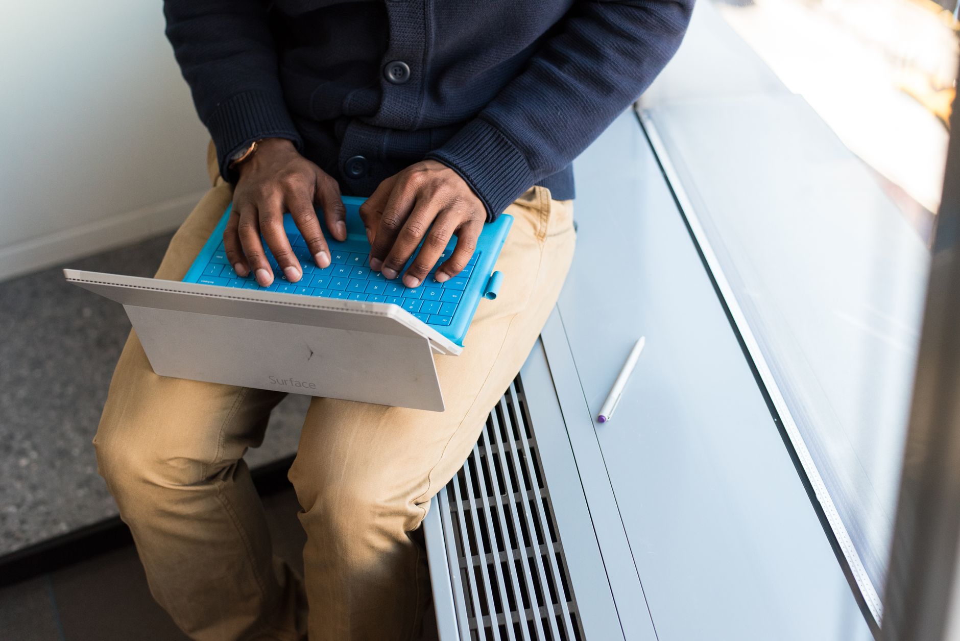 Man in an office setting working remotely on laptop next to a large window.